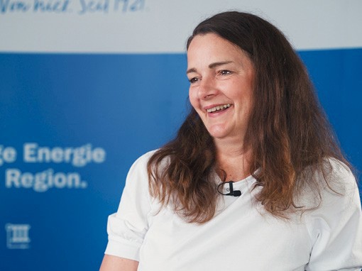 Frau mit dunklen langen Haaren lächelt erfreut.