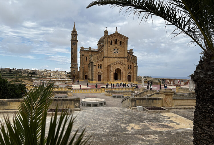 Kirche aus hellem Stein mit großem Vorplatz. Es ist eine Kirche auf der Mittelmeerinsel Gozo.