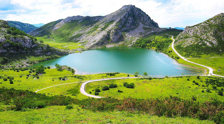 Ein türkis schimmernder See in der Mitte des Bildes. Drumherum grüne, hügelige Landschaft, die von kleinen Wegen durchzogen ist.